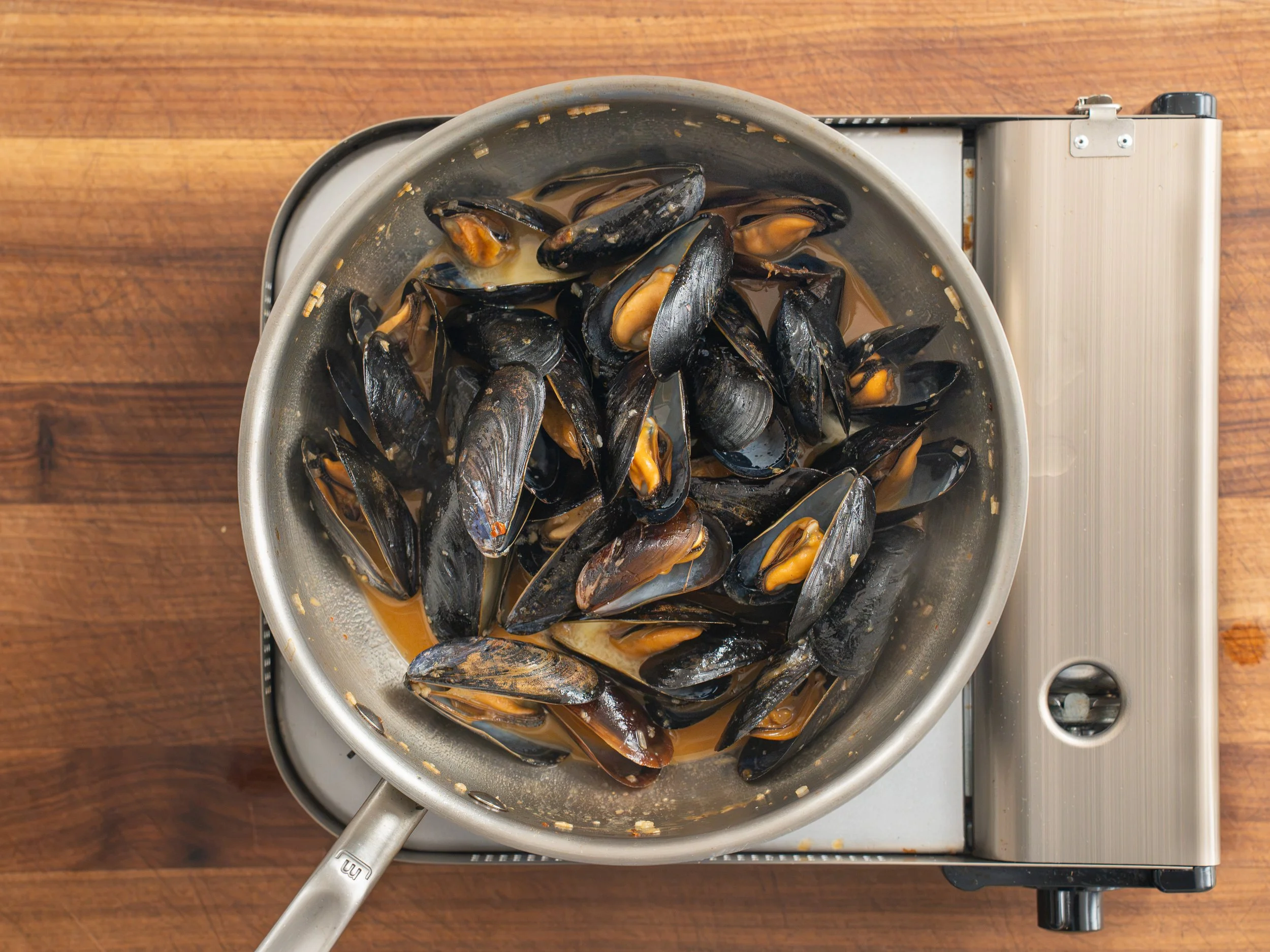 cooked mussels sitting in silver pan of emulsified white wine sauce