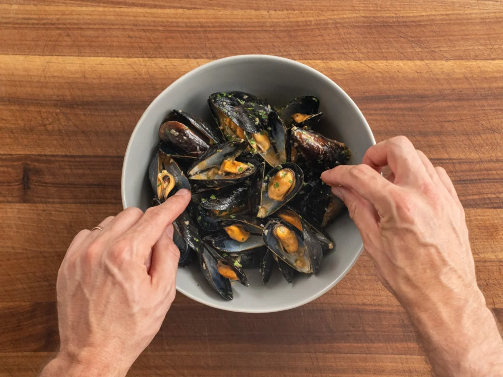man using hands to arrange cooked mussels in grey serving bowl