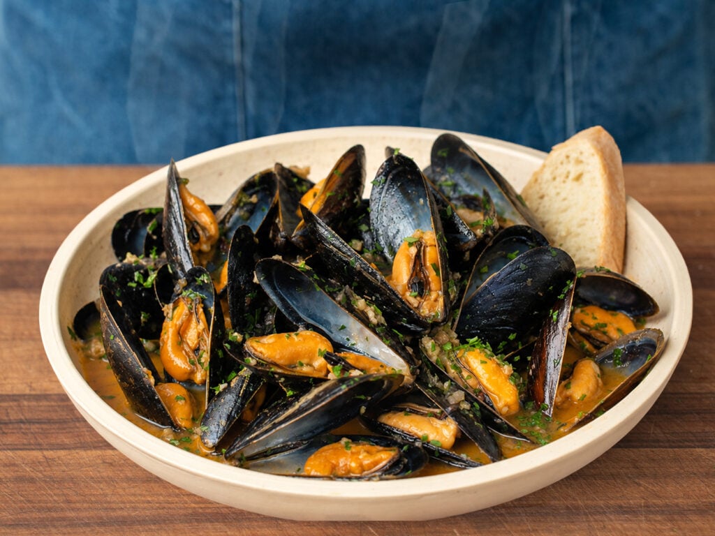 cream colored bowl filled with mussels in white wine sauce garnished with chopped parsley and bread