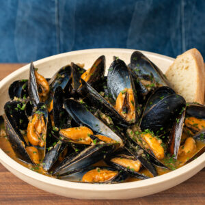 cream colored bowl filled with mussels in white wine sauce garnished with chopped parsley and bread