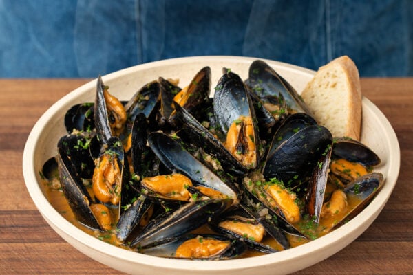 cream colored bowl filled with mussels in white wine sauce garnished with chopped parsley and bread