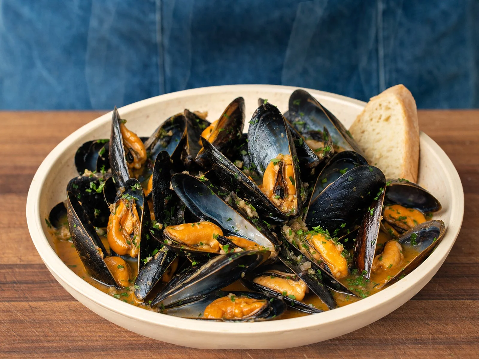 bowl of finished mussels in white wine sauce garnished with chopped parsley and bread