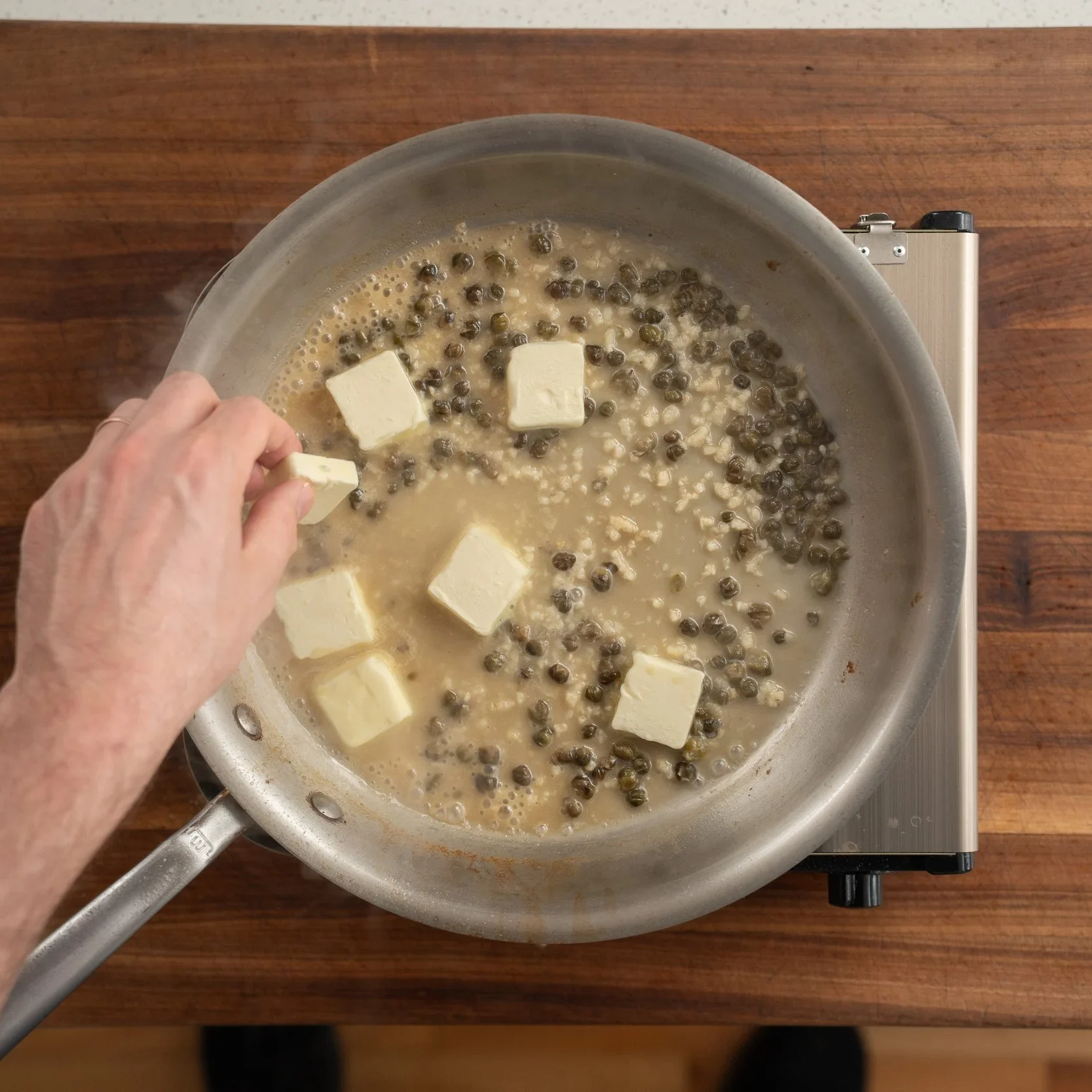 adding pads of butter into white wine caper sauce