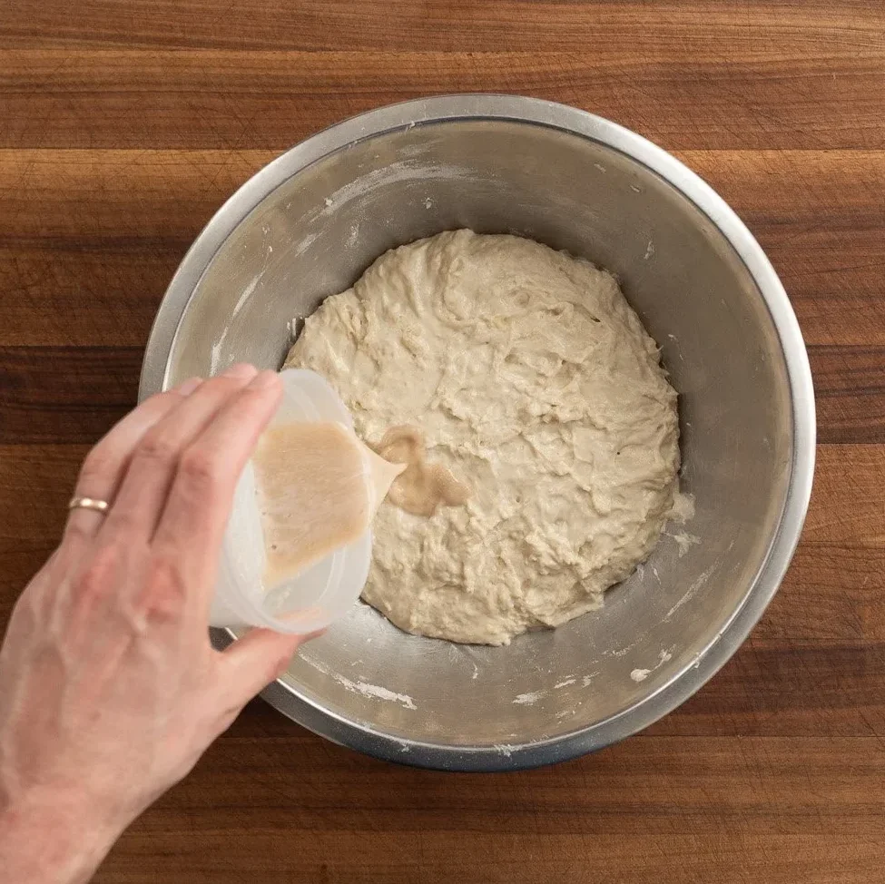 adding yeast and salt to wet dough in mixing bowl