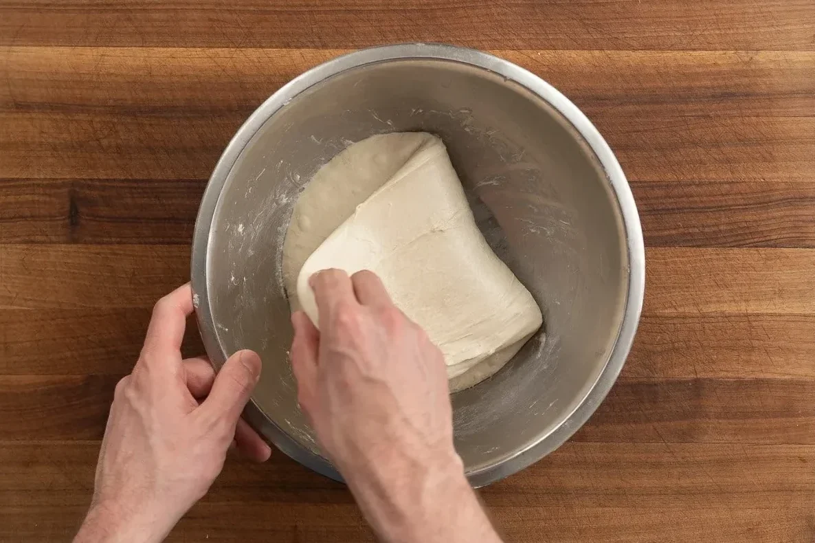 folding over focaccia dough in metal bowl