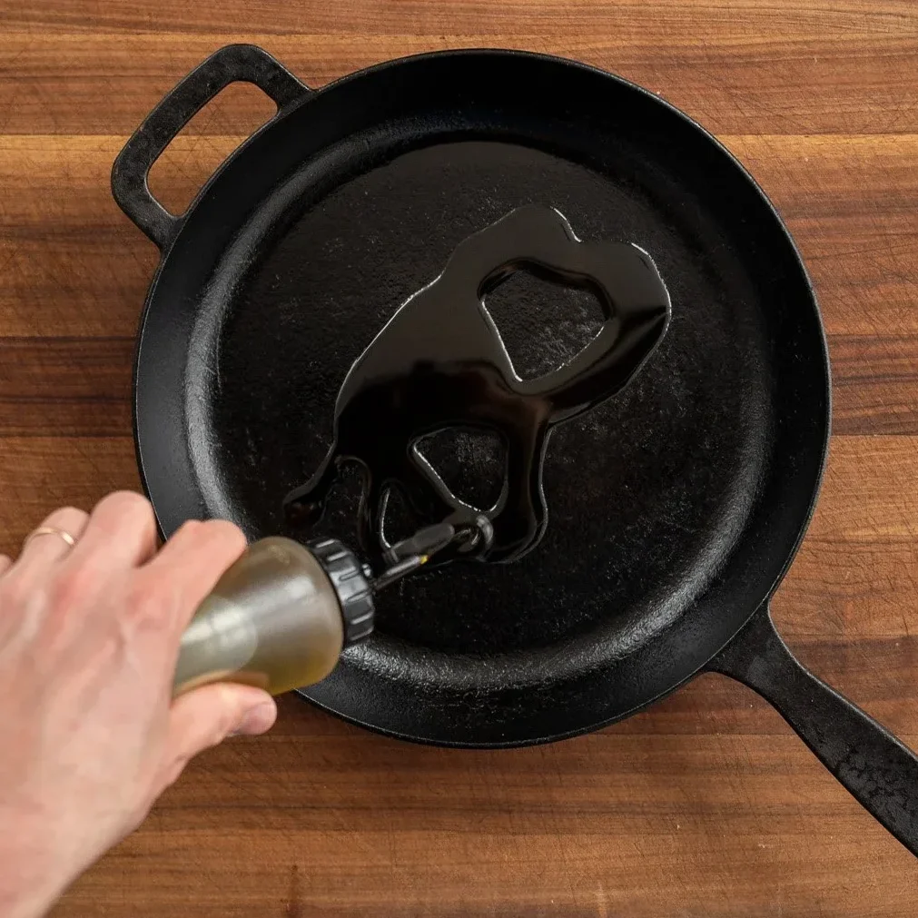 adding olive oil to a cast iron pan using a squeeze bottle