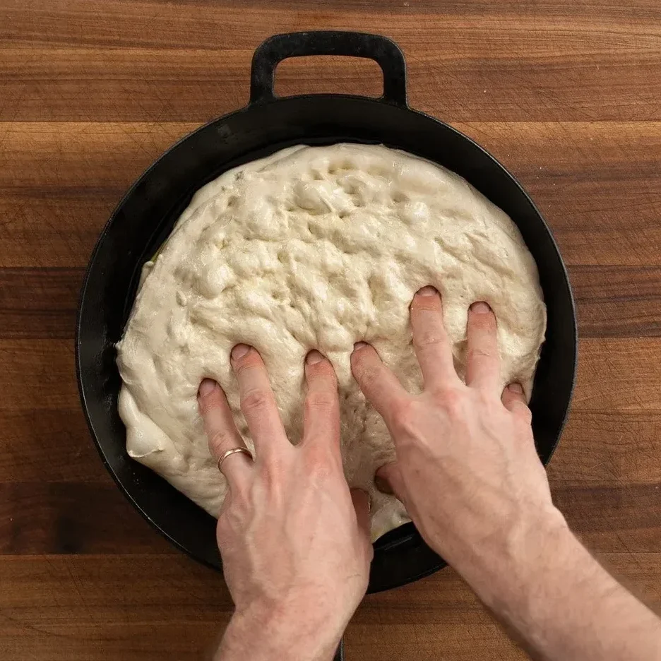 dimpling focaccia dough in cast iron pan