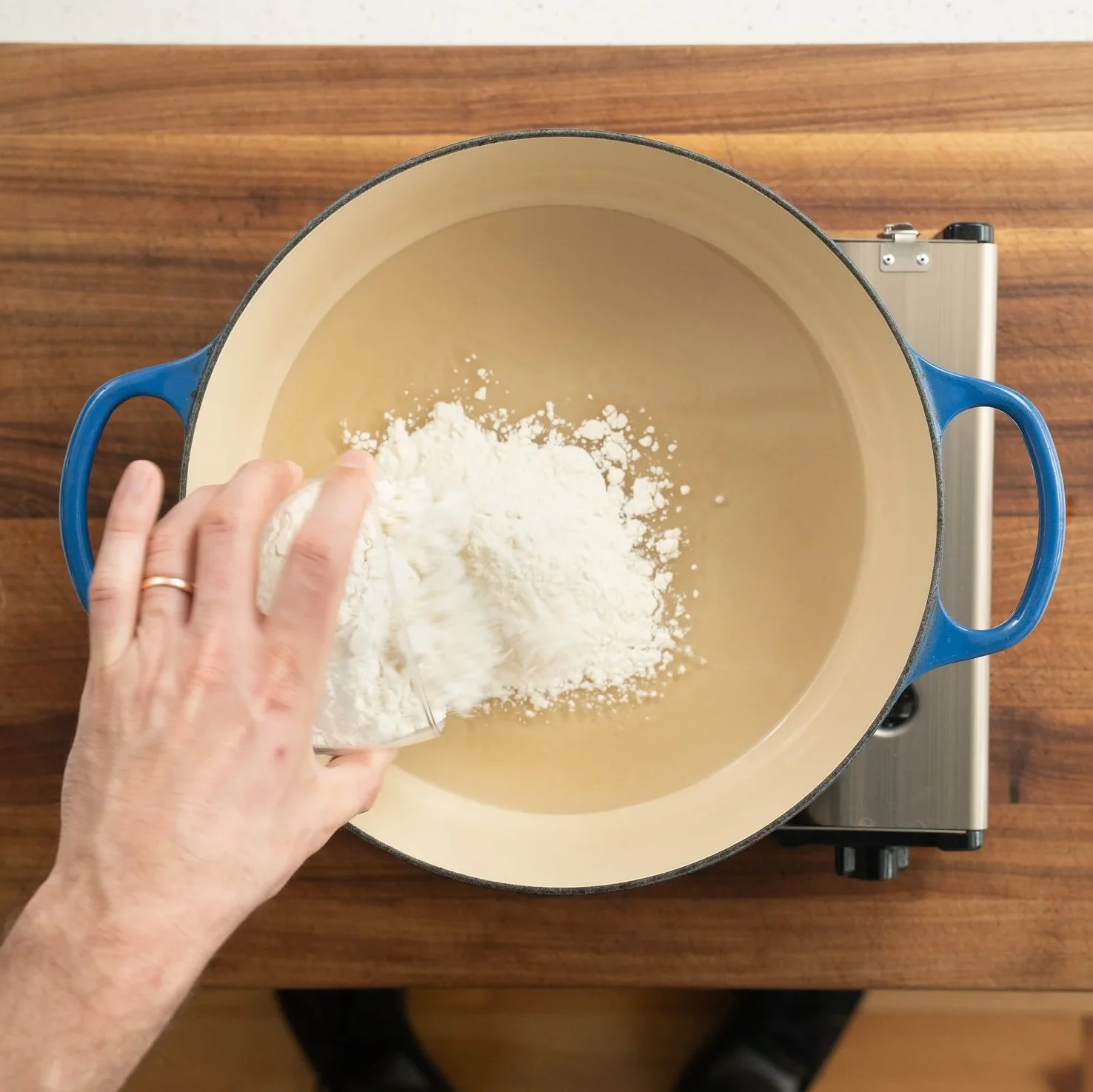 adding flour into oil in a blue dutch oven