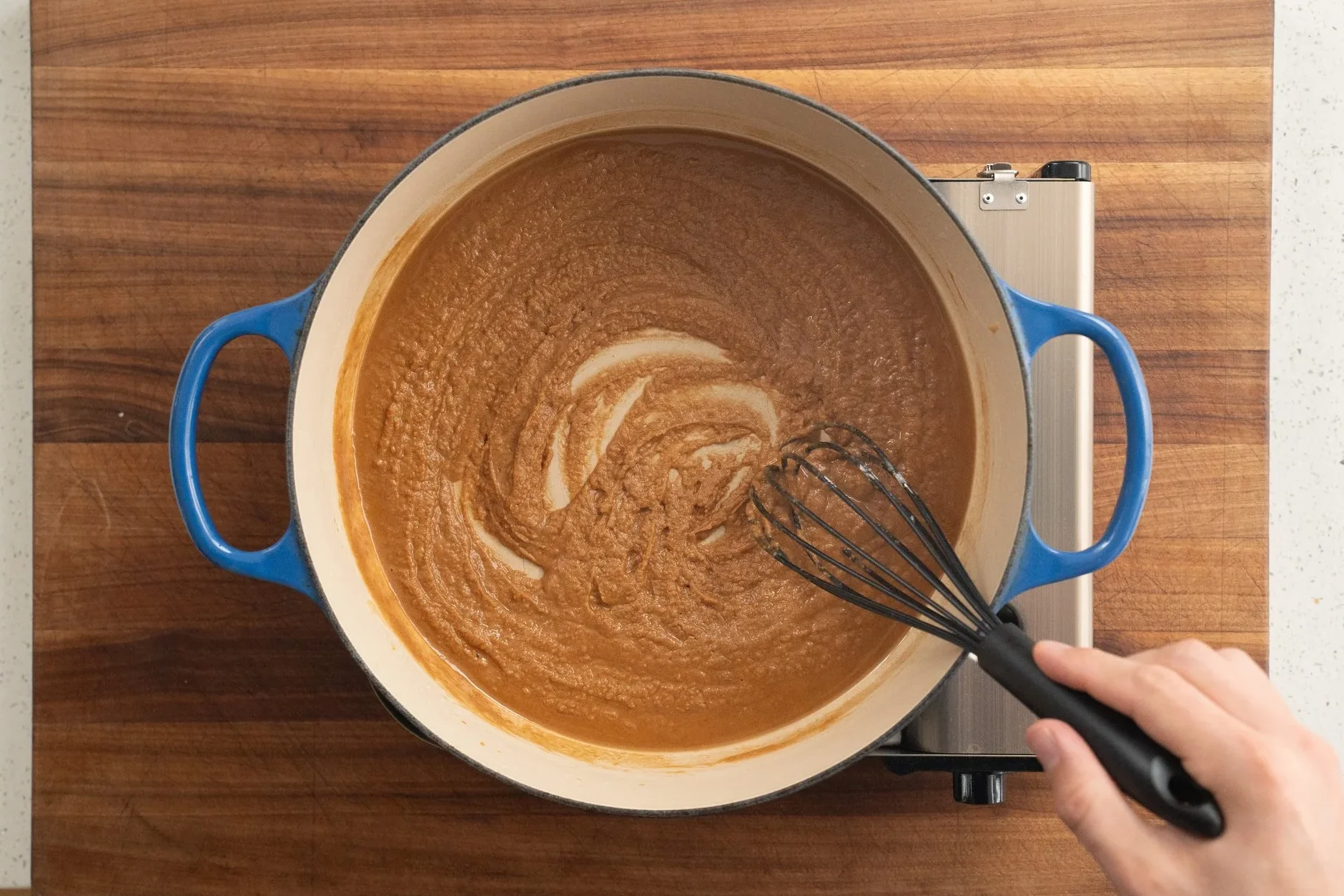 whisking brown roux with black whisk in blue dutch oven