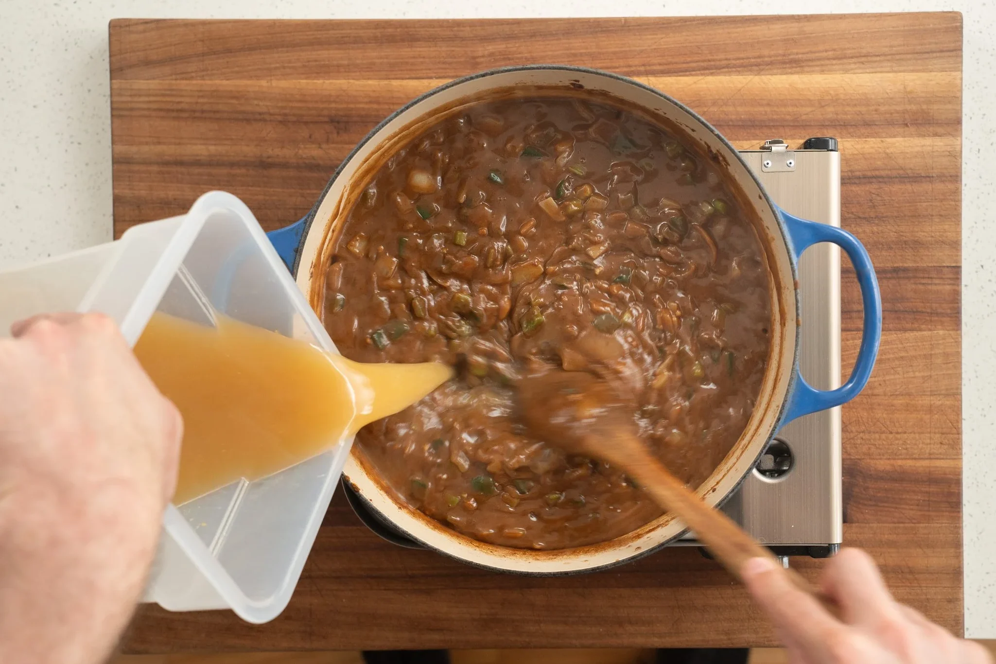 adding chicken stock to a gumbo base in a blue dutch oven