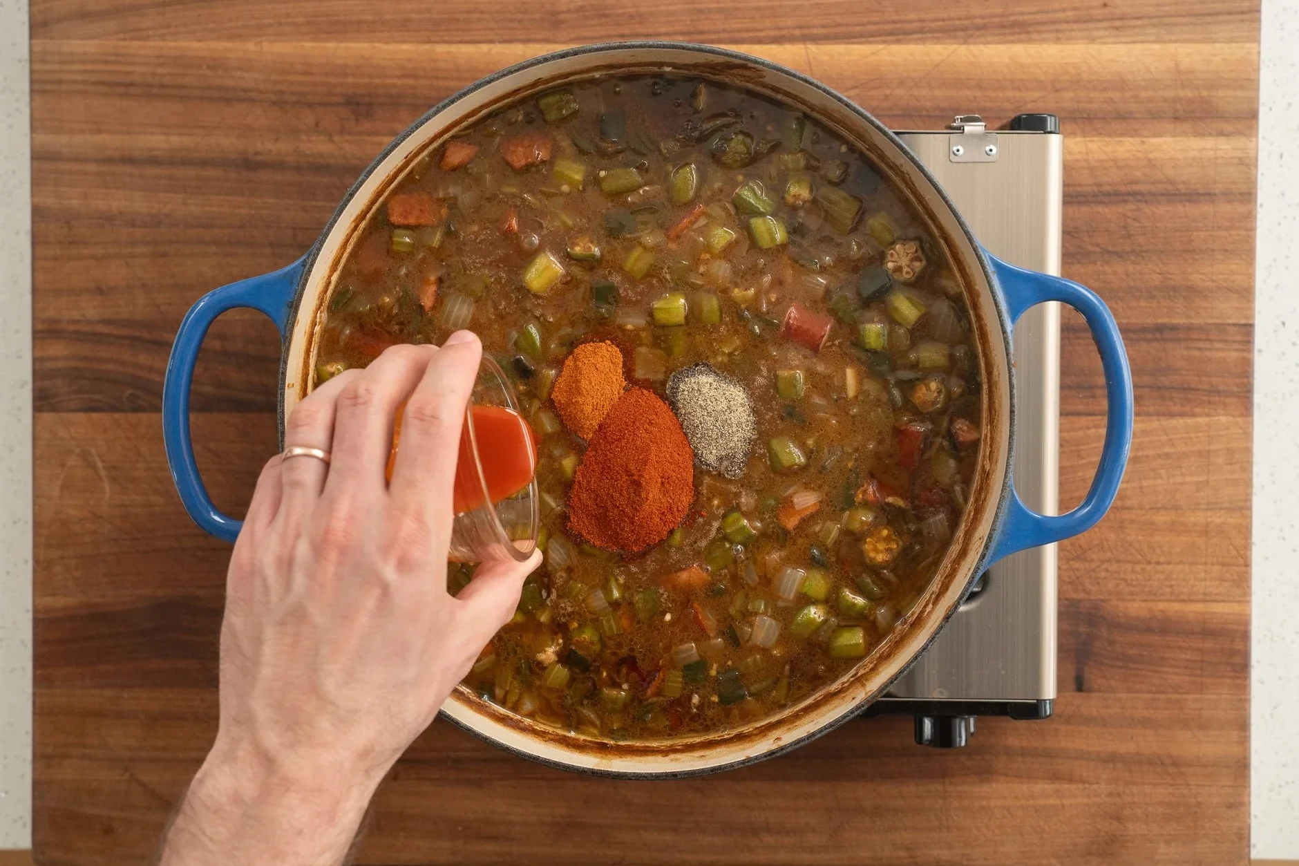 adding spice blend to gumbo in a blue dutch oven