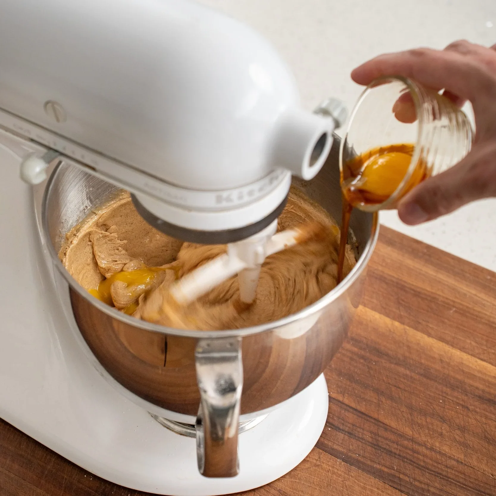adding egg into the bowl of a white stand mixer