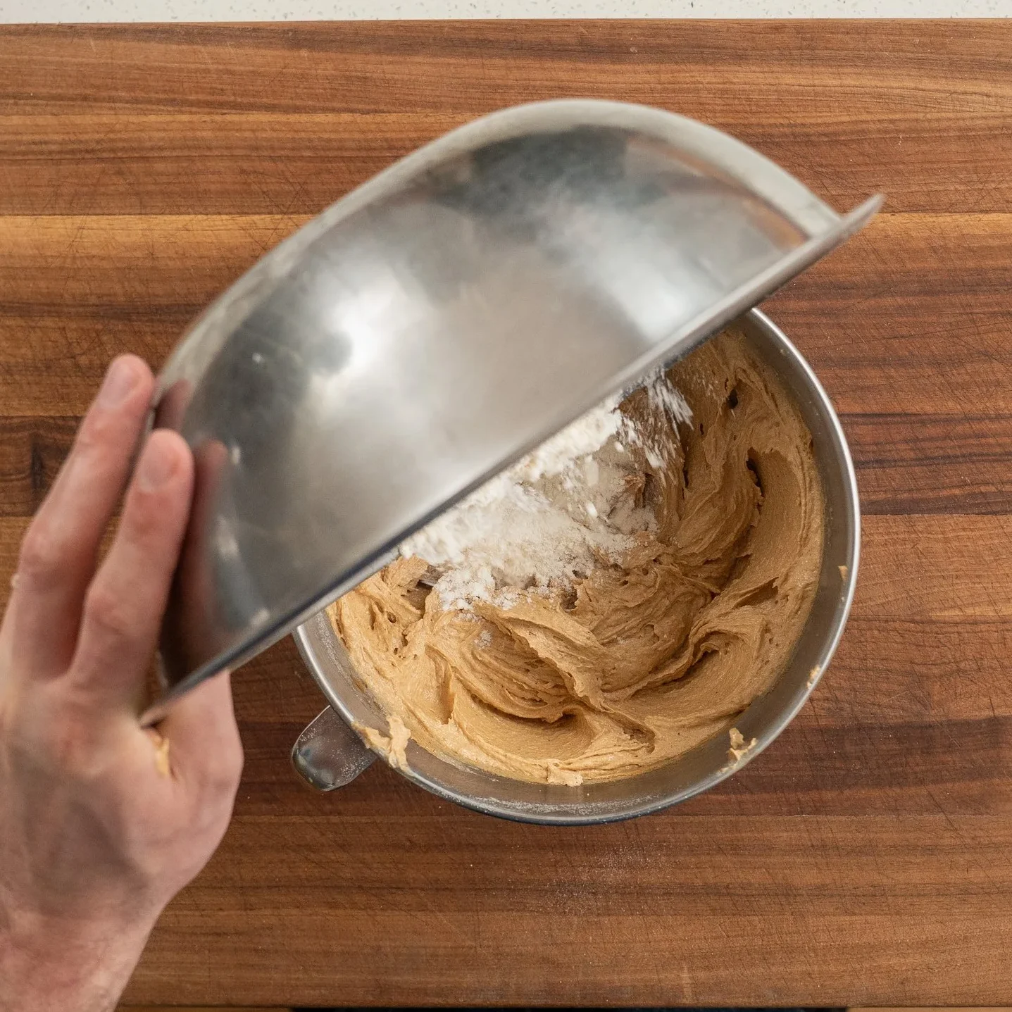 adding dry ingredients into creamed wet ingredients for peanut butter cookies