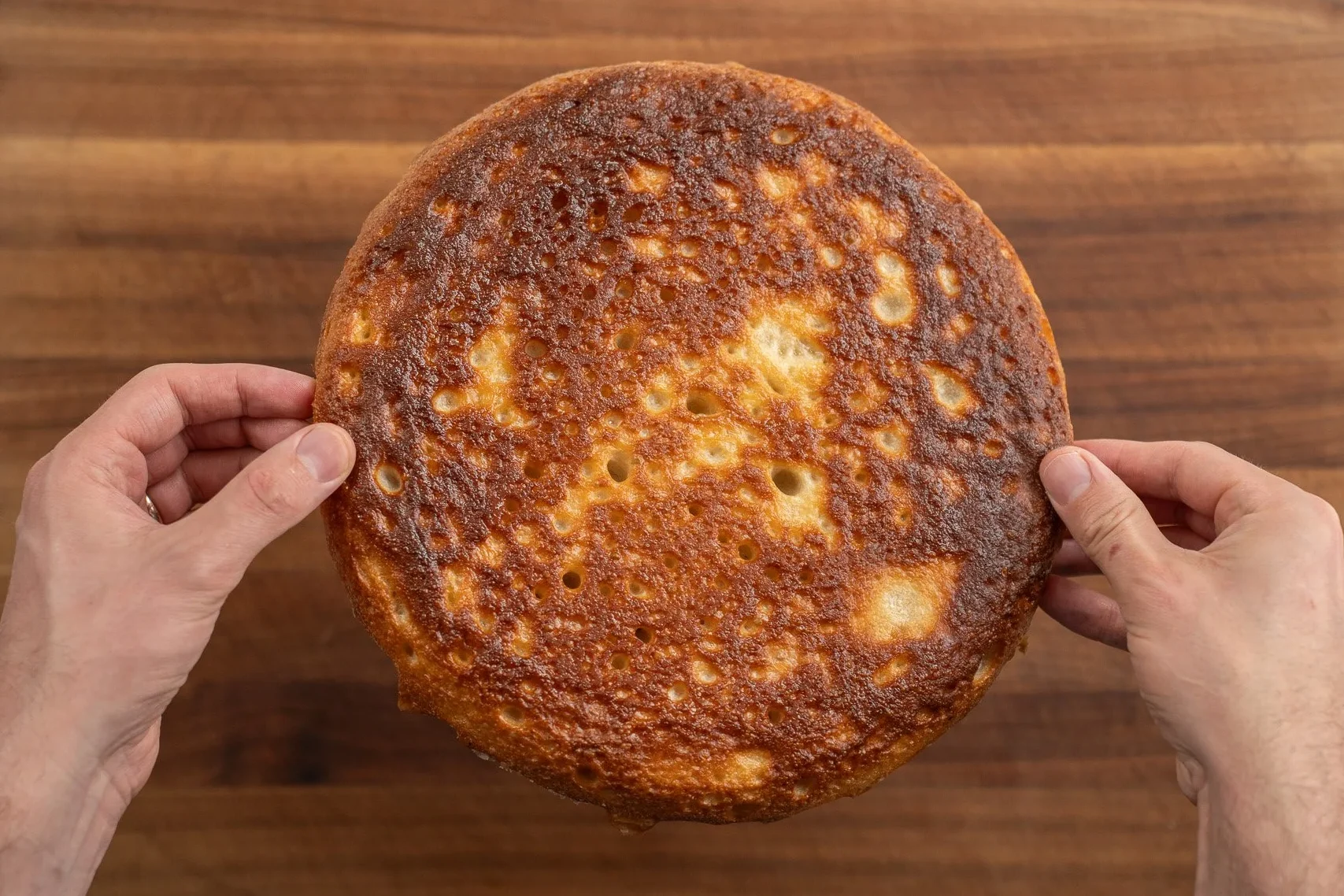 hands holding baked round focaccia upside down to show golden brown bake on bottom