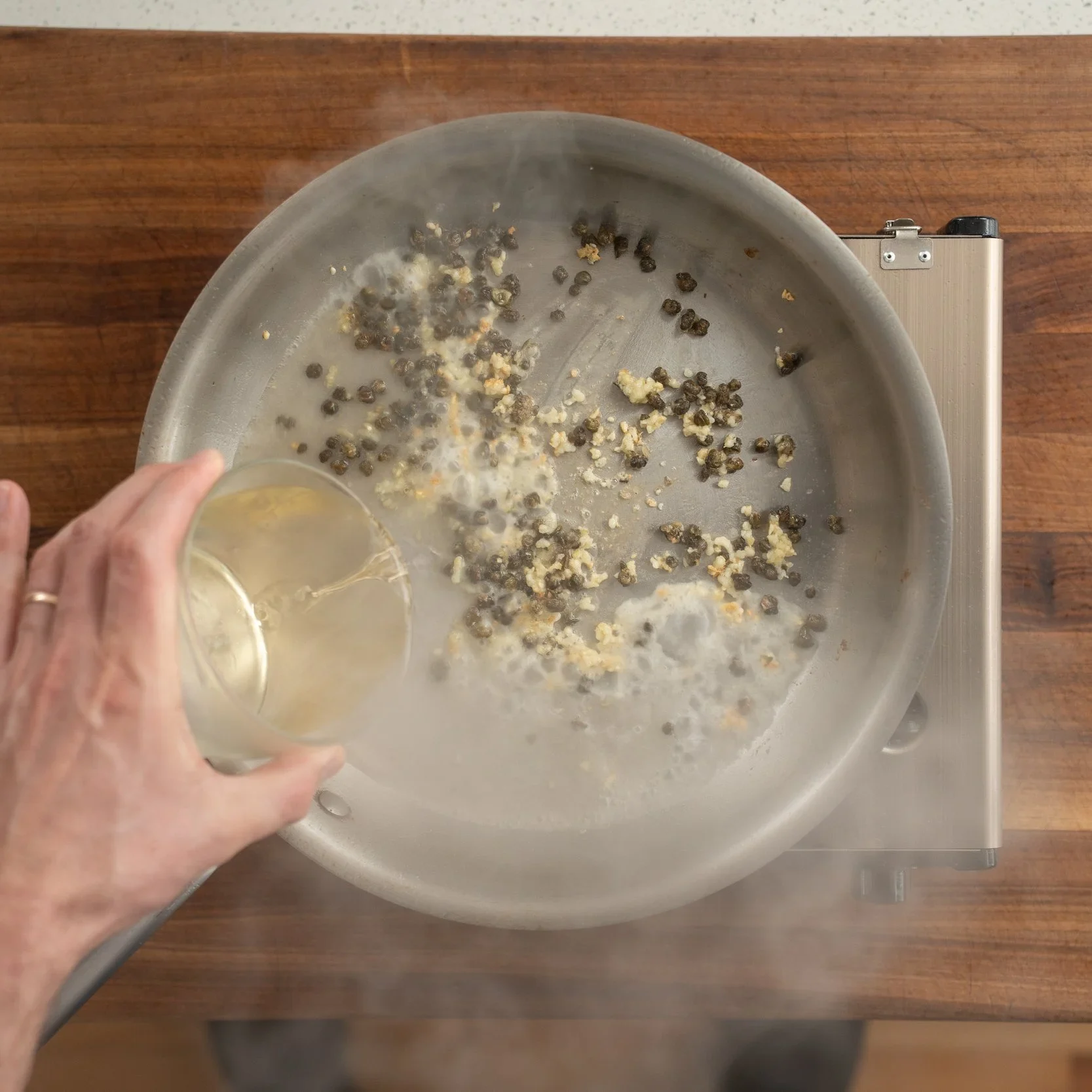 adding white wine to garlic and capers in pan