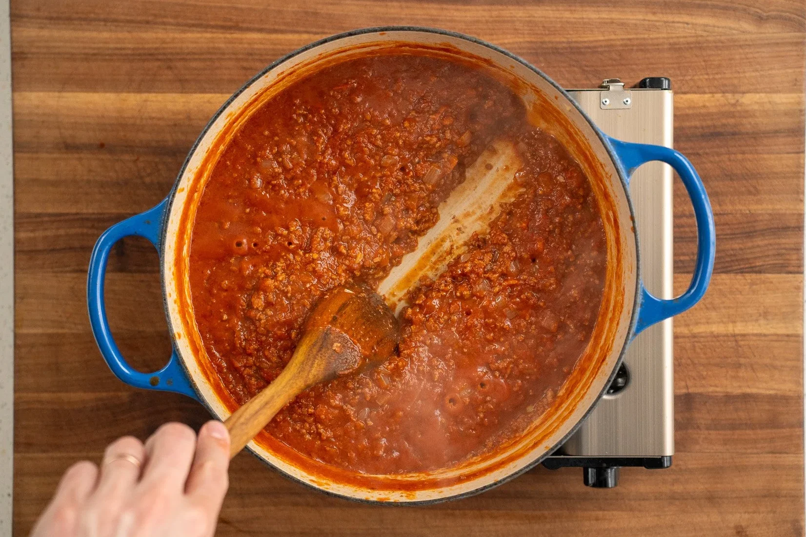 cooked meat sauce in a blue dutch oven with wooden spoon leaving a trail