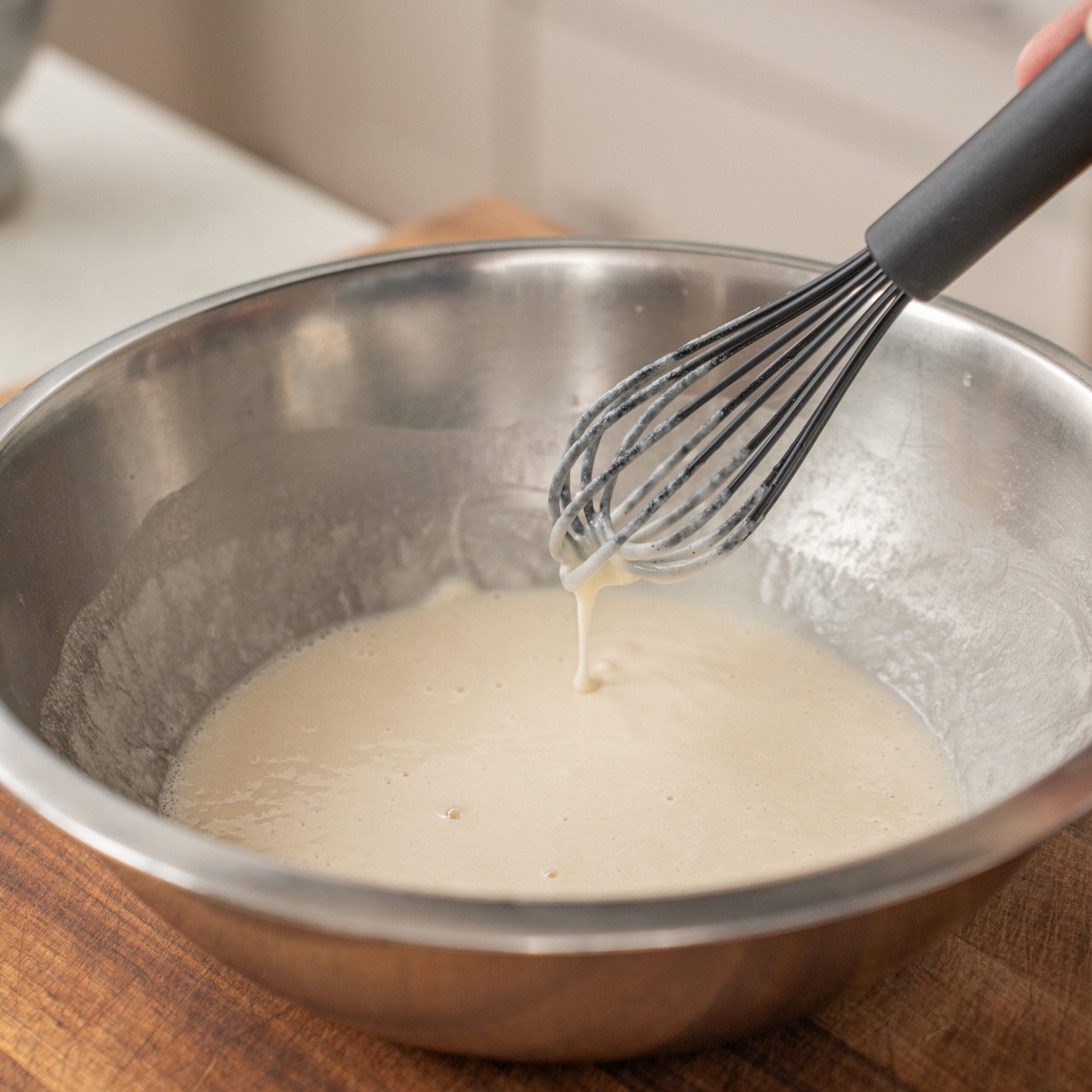 small black whisk being lifted from silver bowl of beer batter