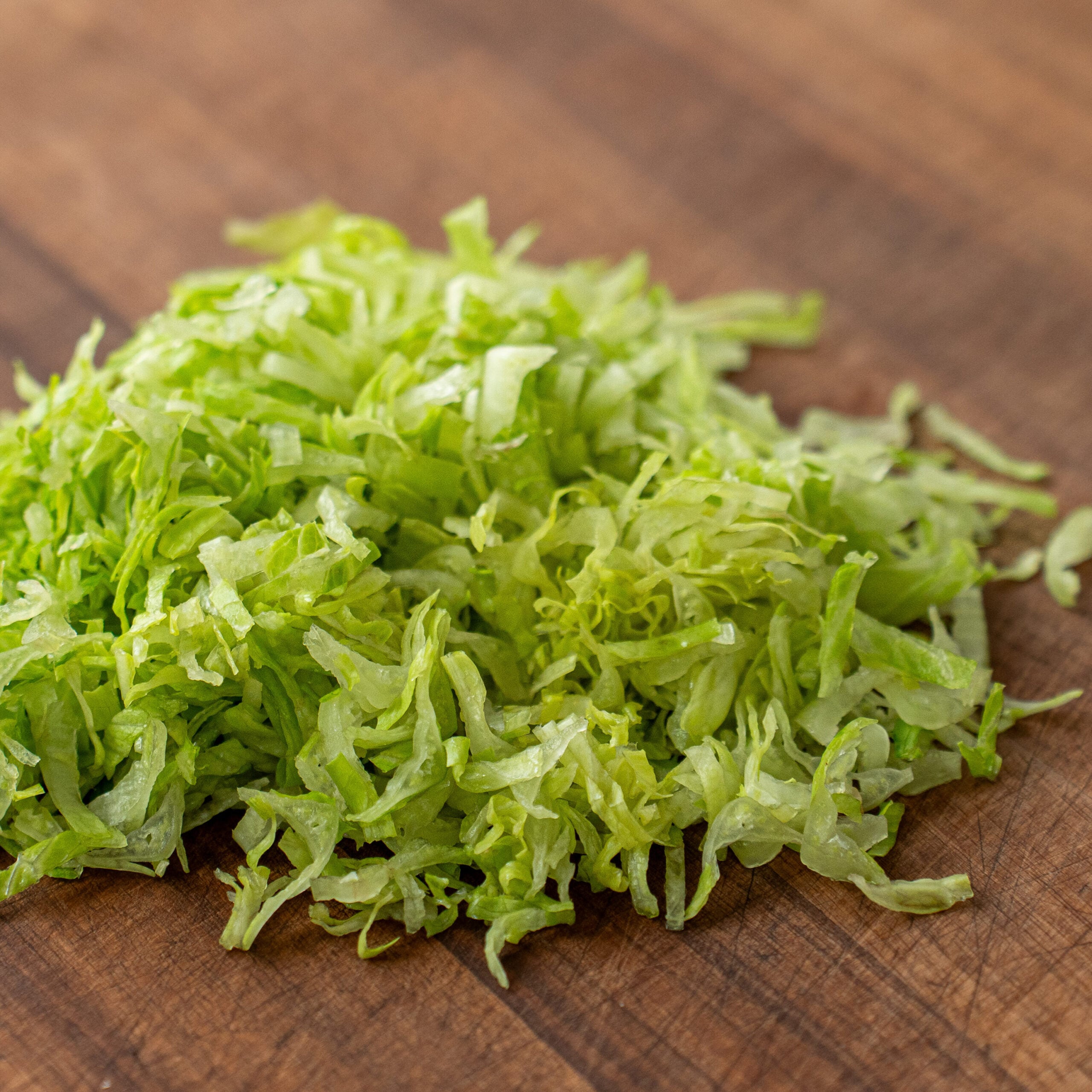 pile of shredded green lettuce on wood cutting board