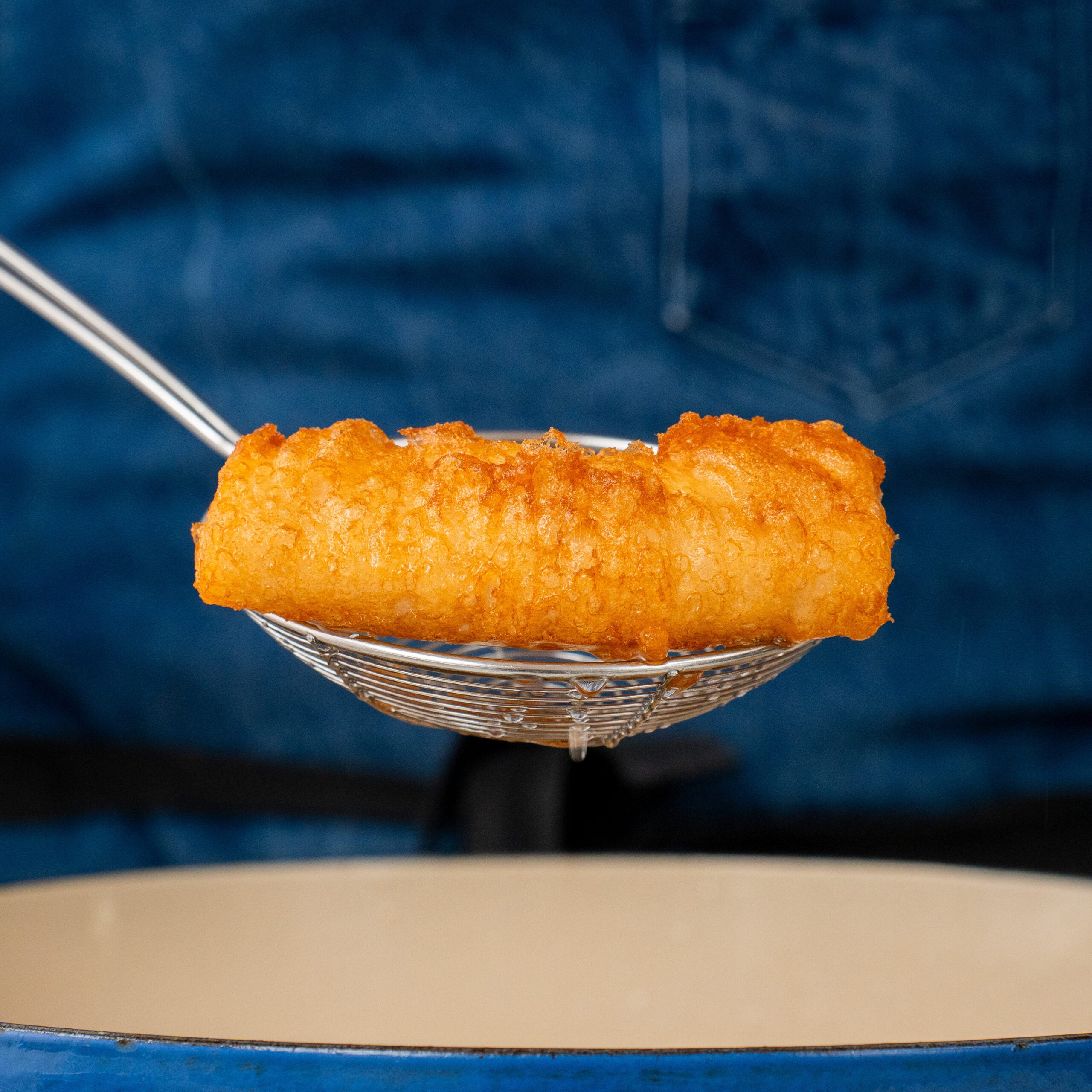 spider strainer lifting piece of beer battered fish from blue dutch oven