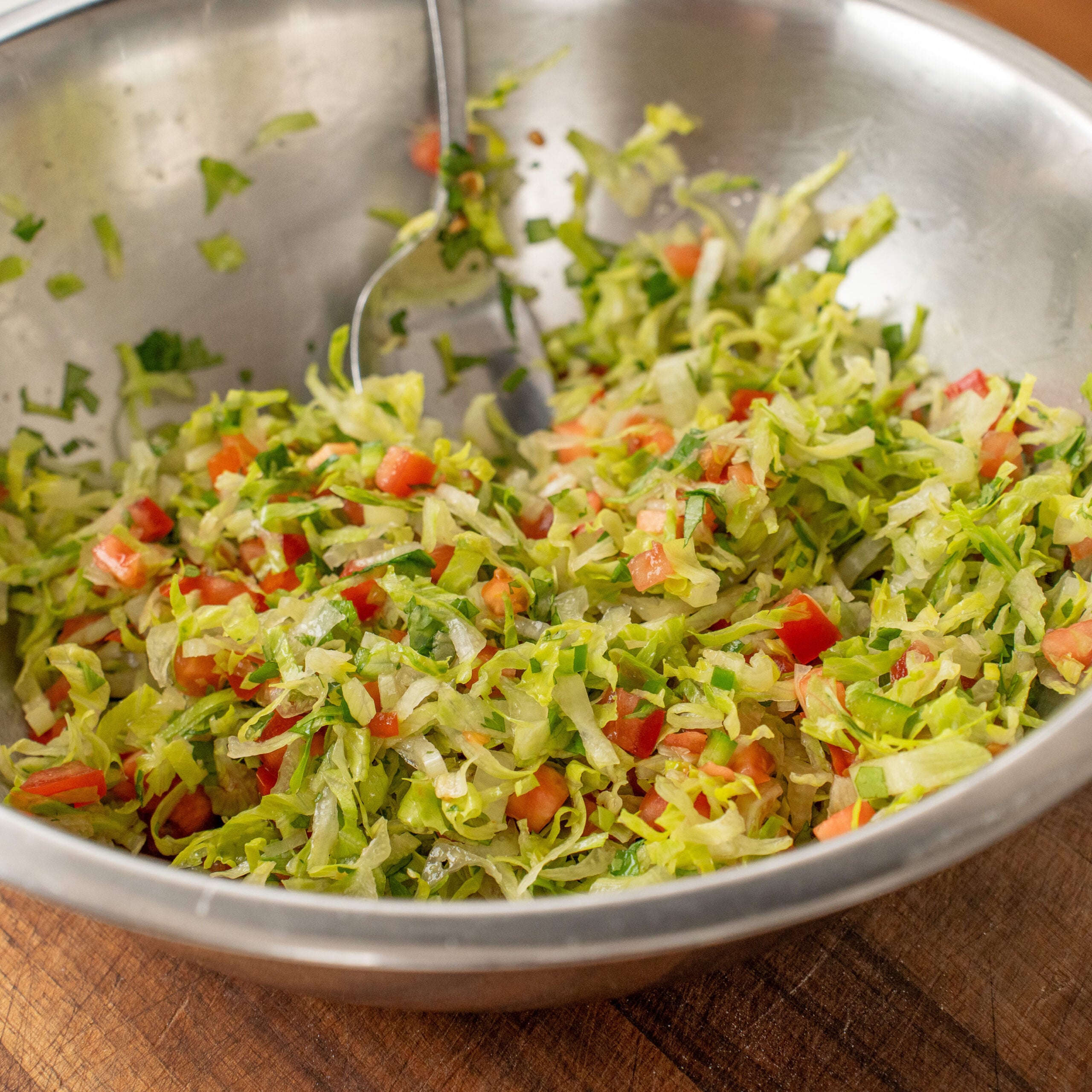 silver bowl filled with mixture of dressed shredded lettuce tomato