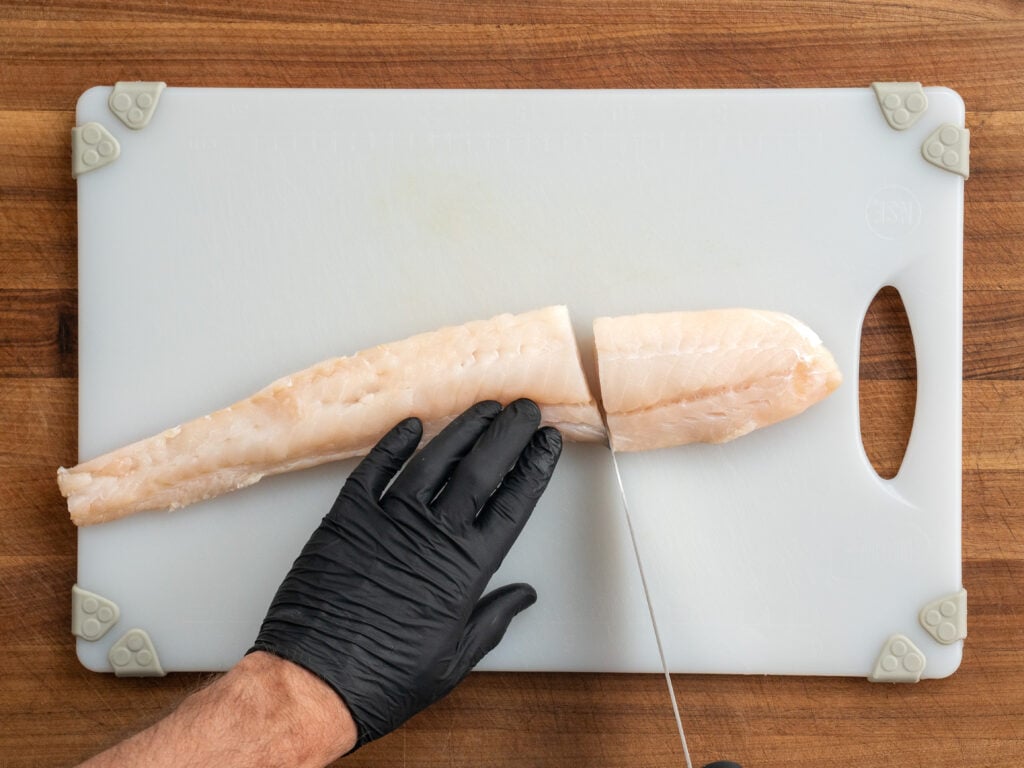 black gloved hand using knife to slice Atlantic cod filet