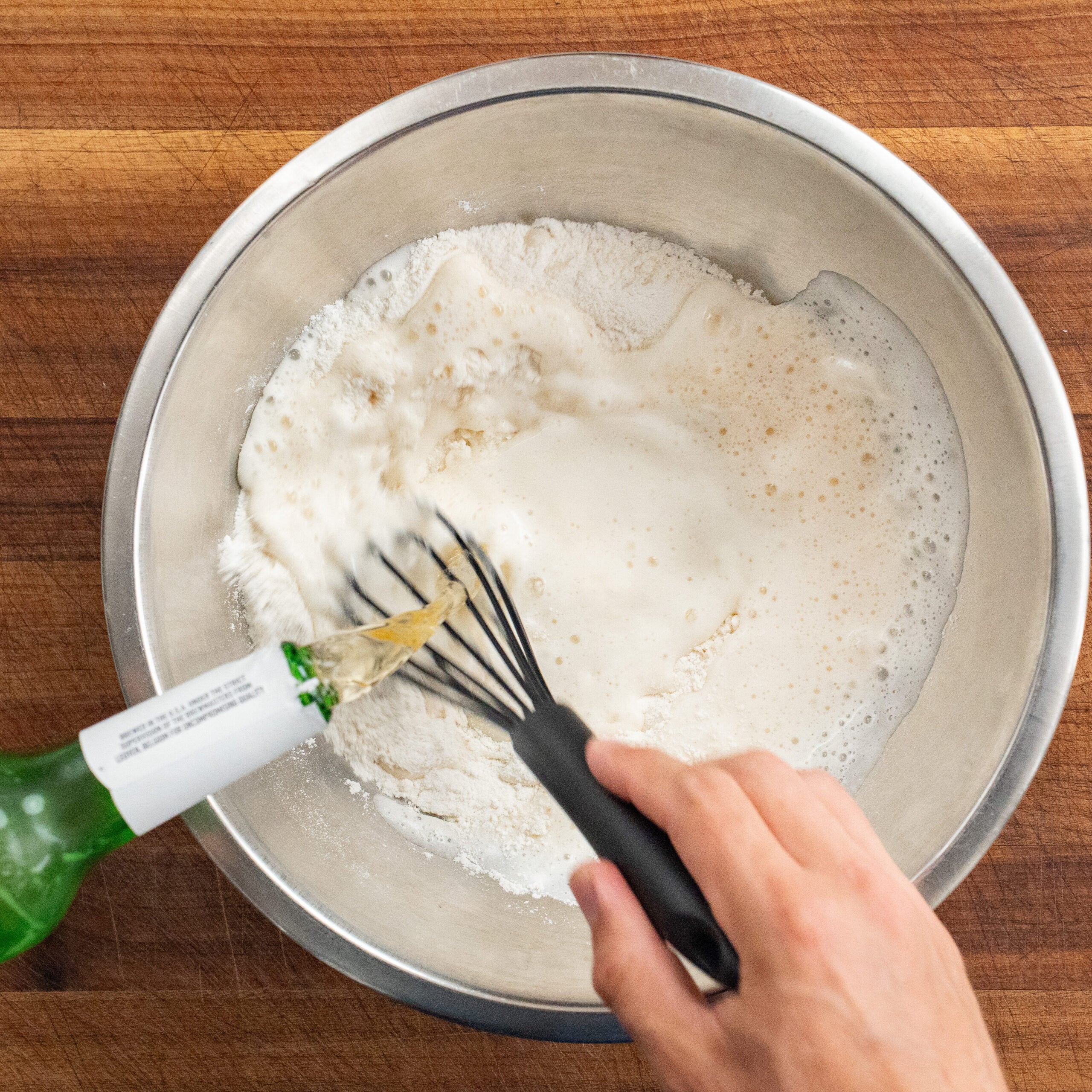hand using black whisk to combine beer with flour to make beer batter