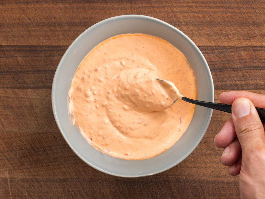 black spoon lifting scoop of sambal mayo from grey bowl