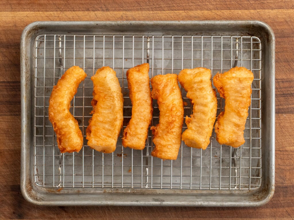 crispy golden brown pieces of cod on wire rack on top of silver sheet tray