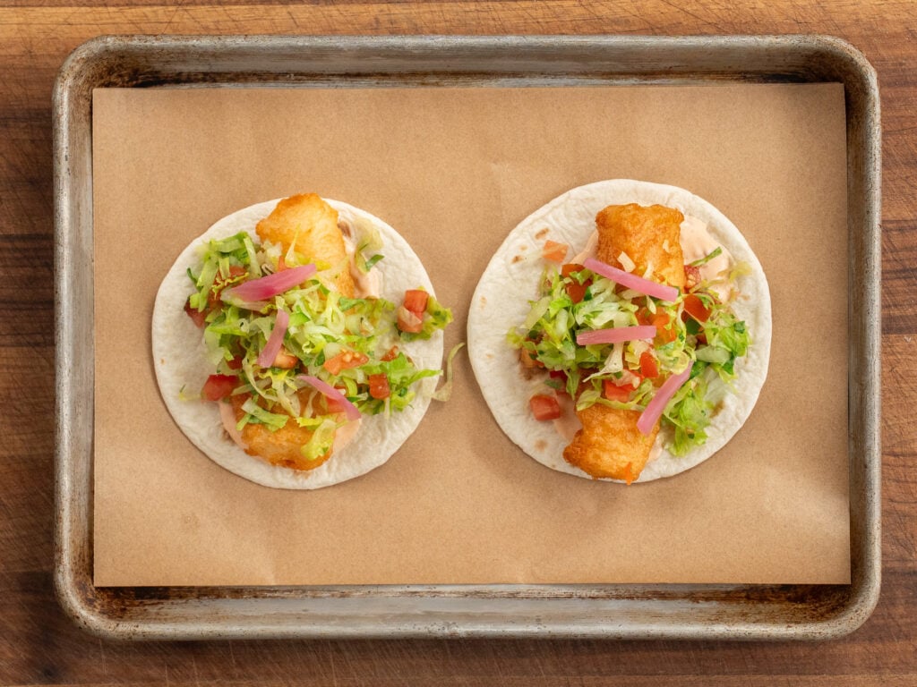 two fried fish tacos topped with salad slaw on parchment lined sheet tray