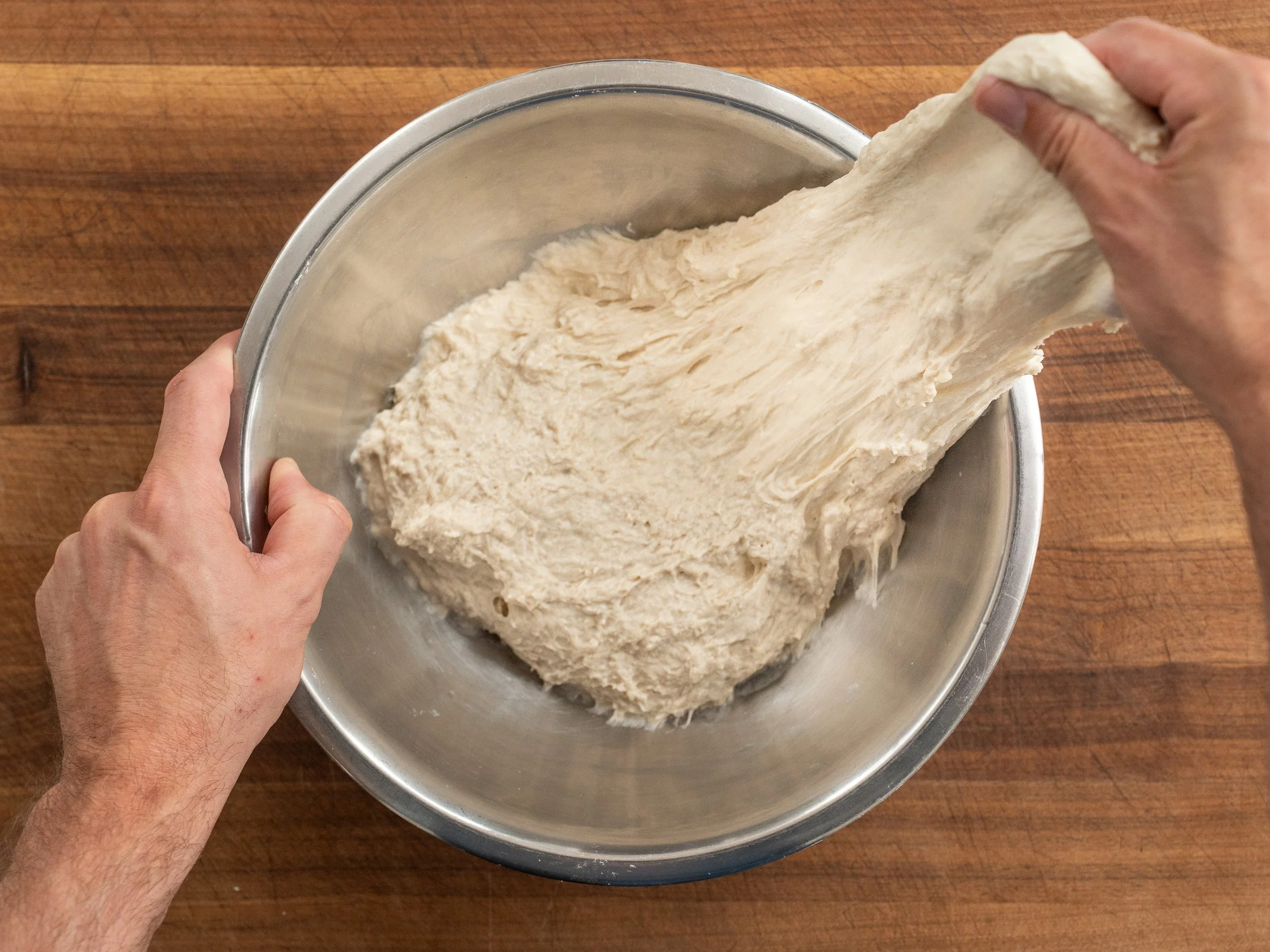 pulling section of shaggy pizza dough in metal bowl 
