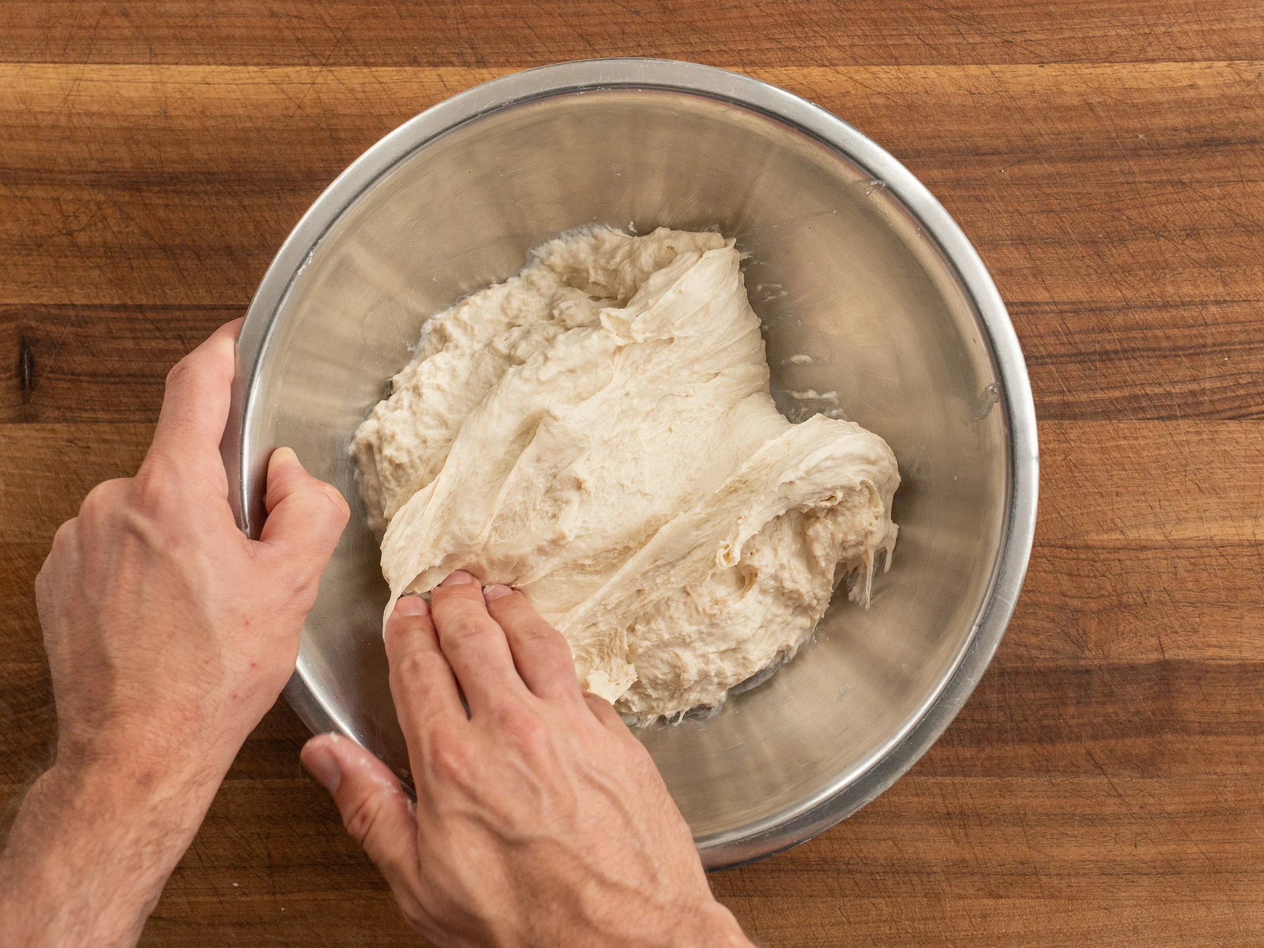 hand pressing down into shaggy ball of dough in metal bowl

