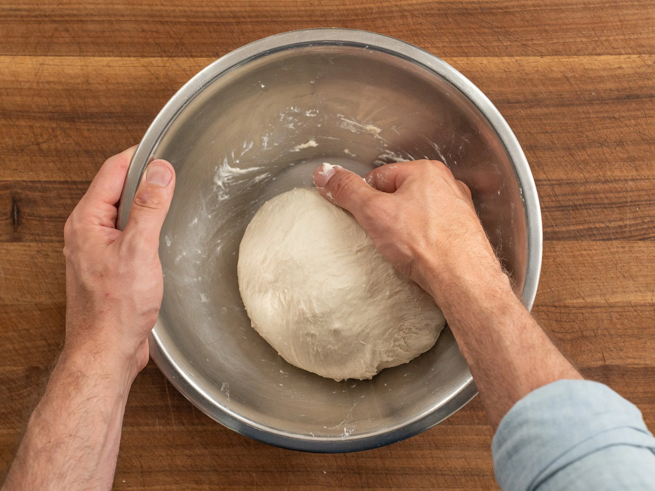 hand routing ball of pizza dough in metal bowl