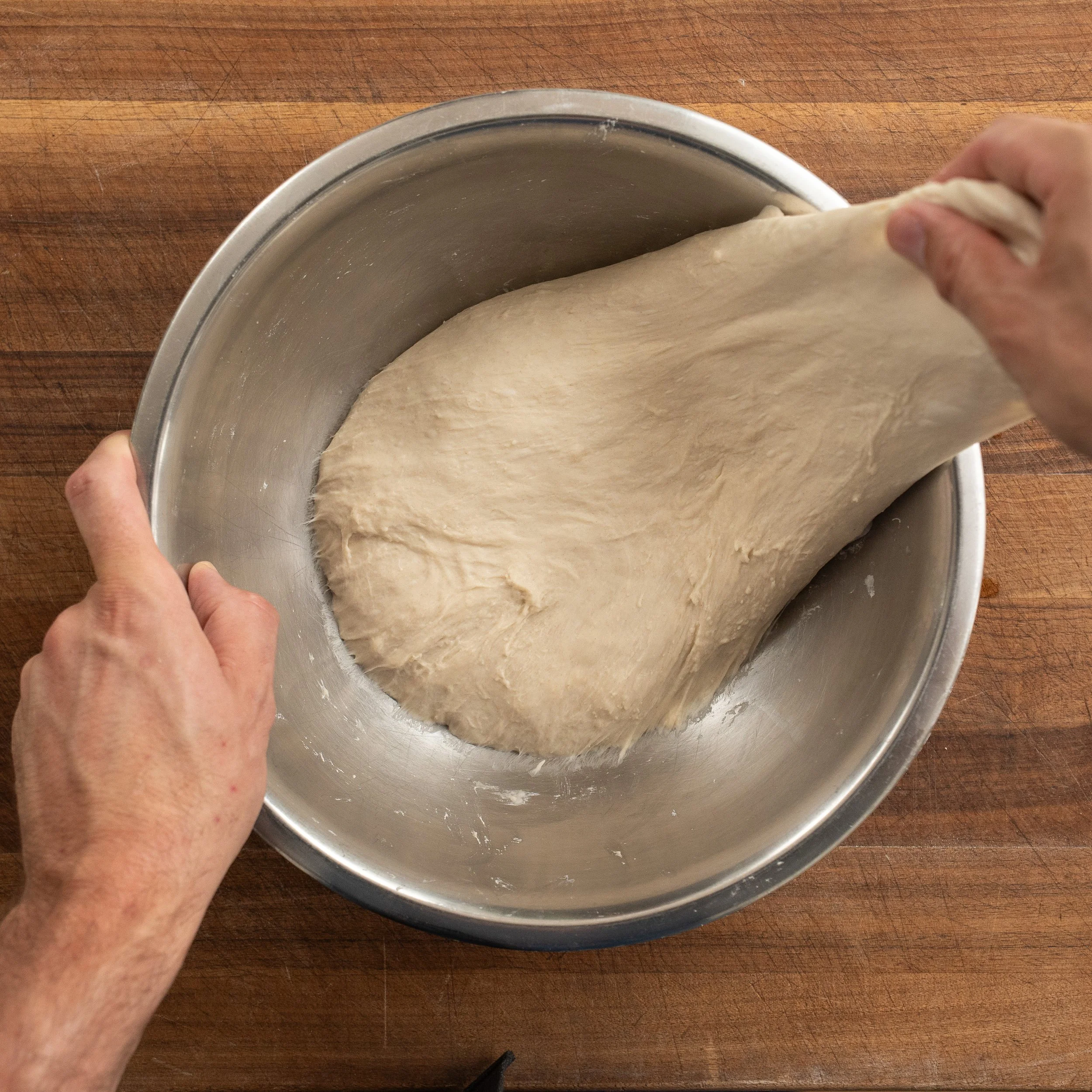 hand pulling out a section of fermented pizza dough