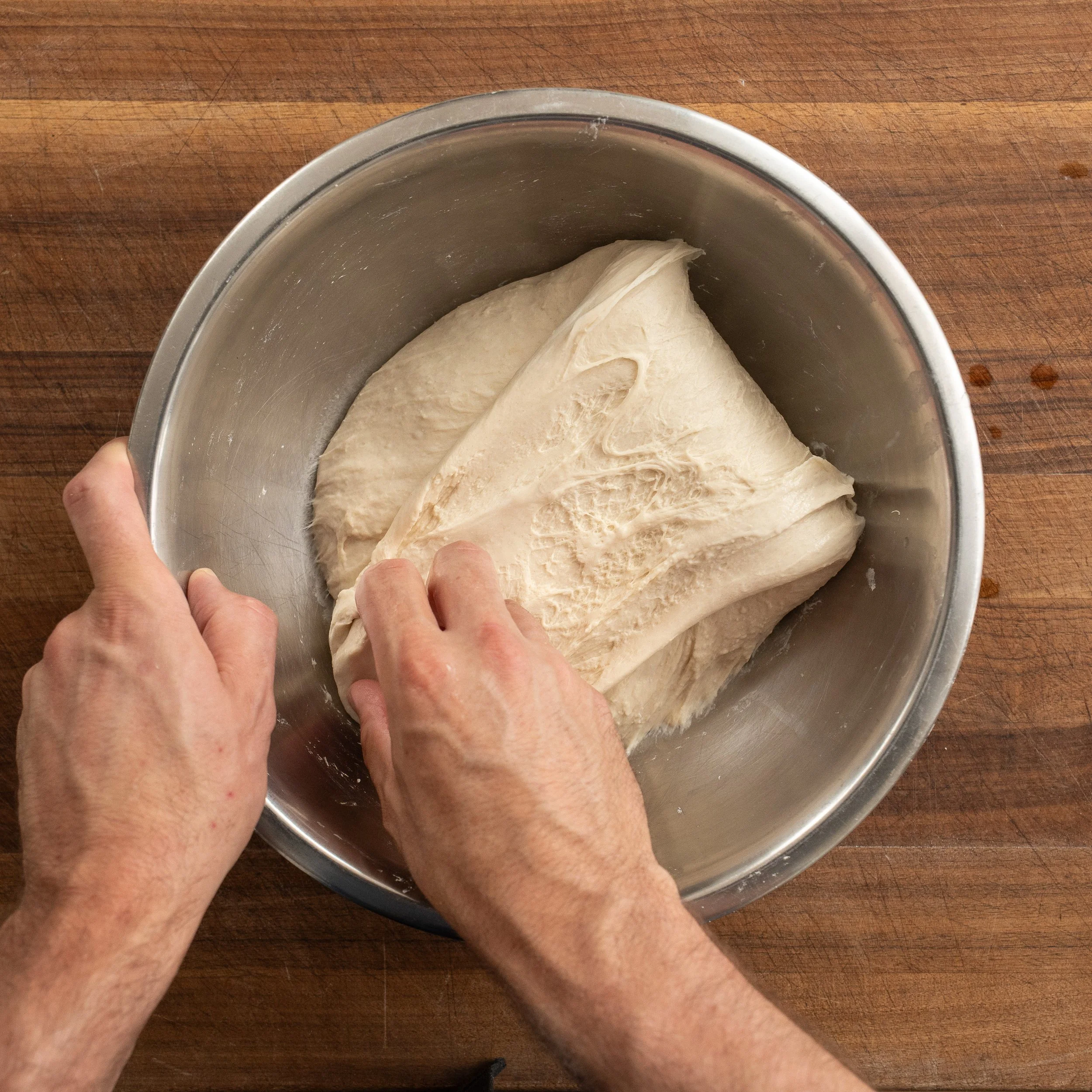 hand pulling section of pizza dough out and folding over 