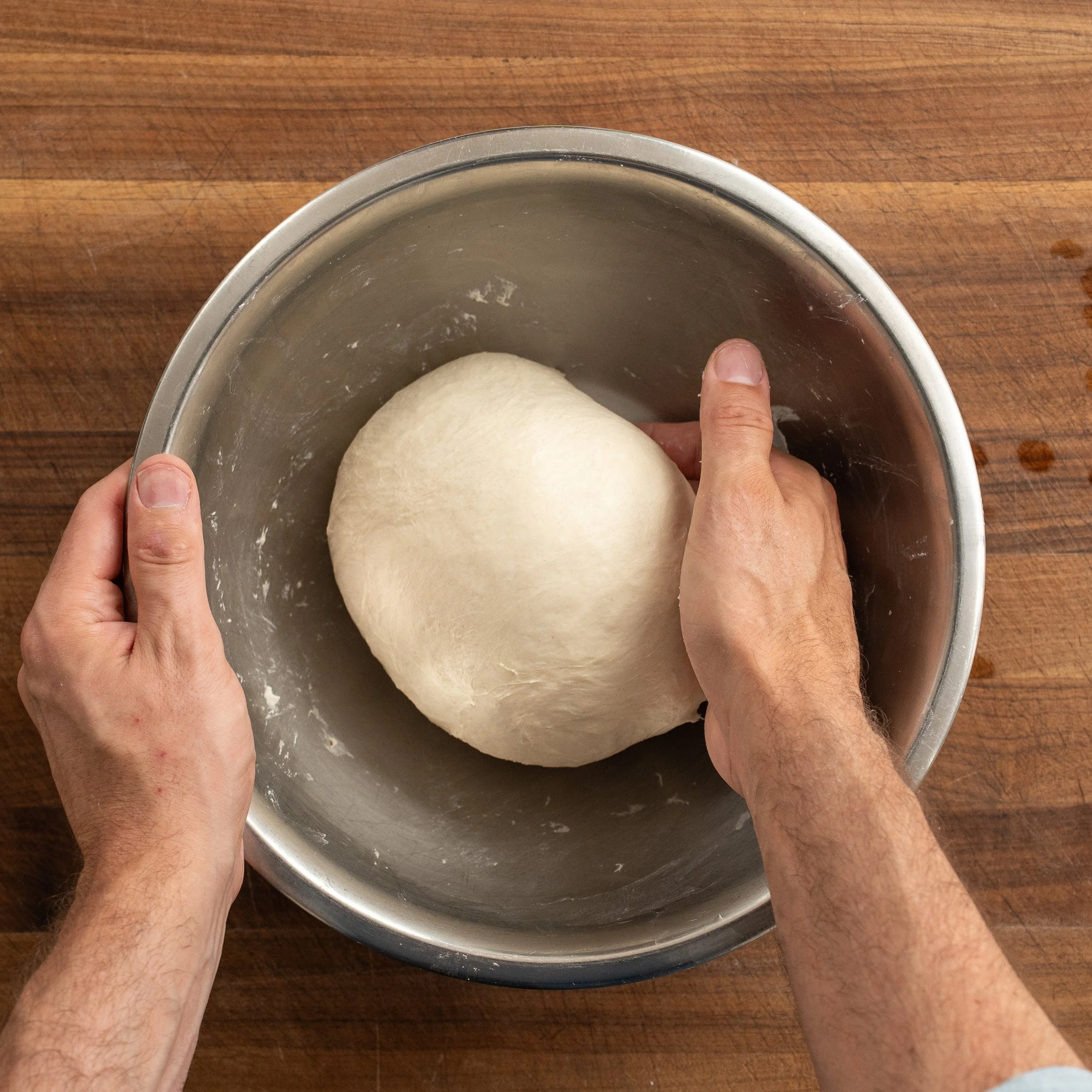 rounding pizza dough ball in metal bowl