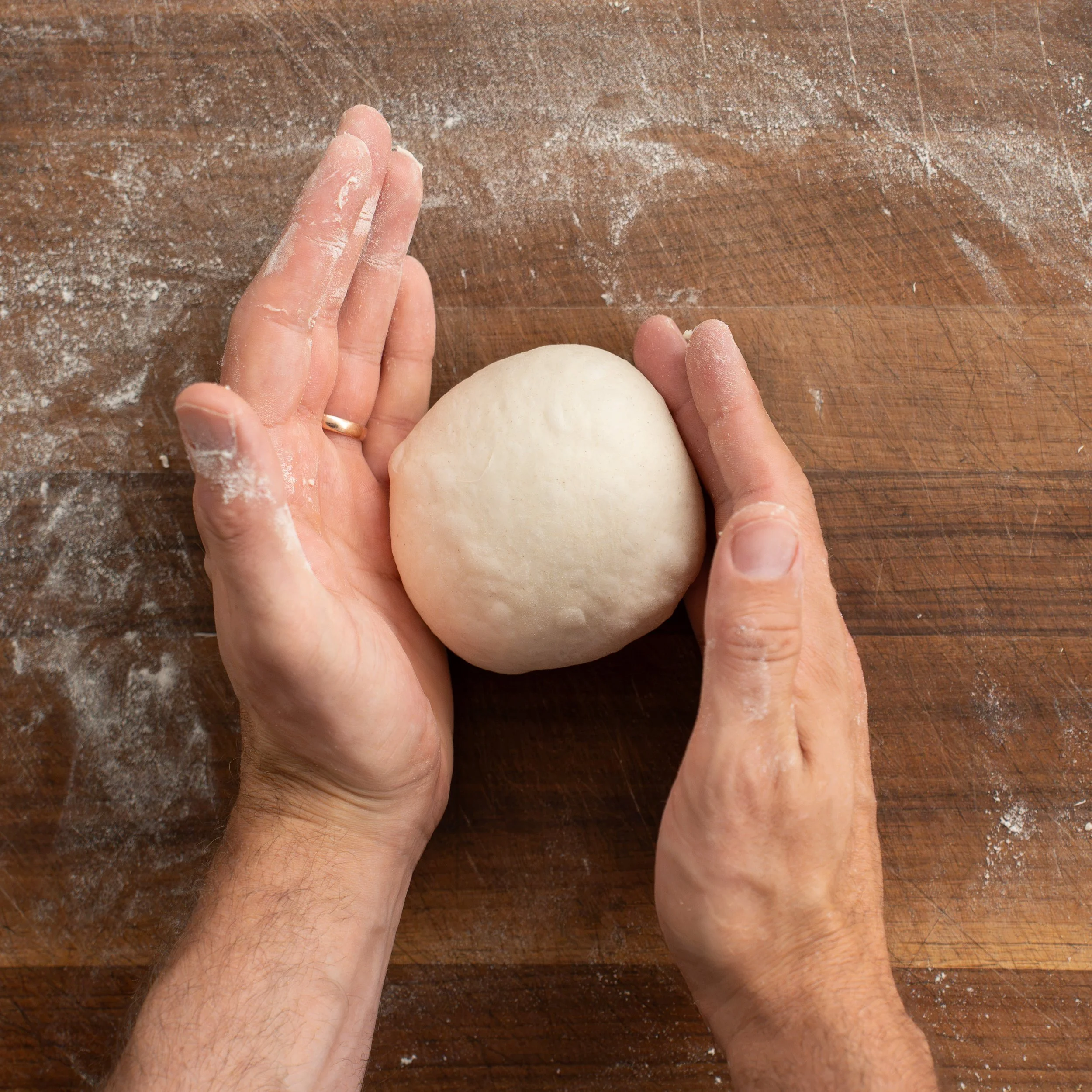 hands rolling pizza dough into small ball