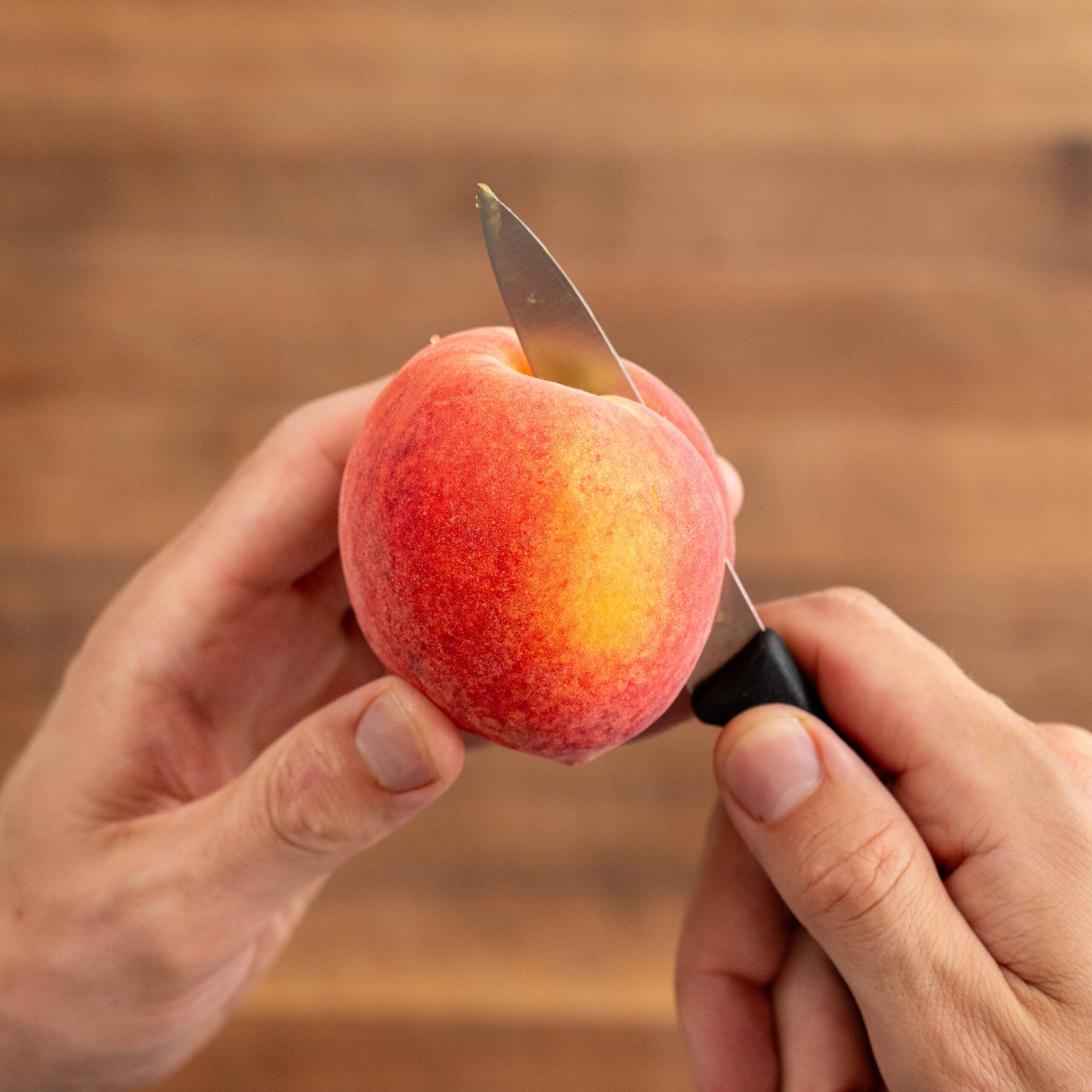 cutting peach in half with small black handle knife