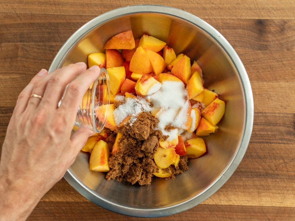 adding sugars to cut raw peaches in bowl