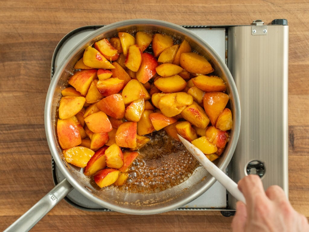 white spatula stirring peaches cooking in silver sauce pan