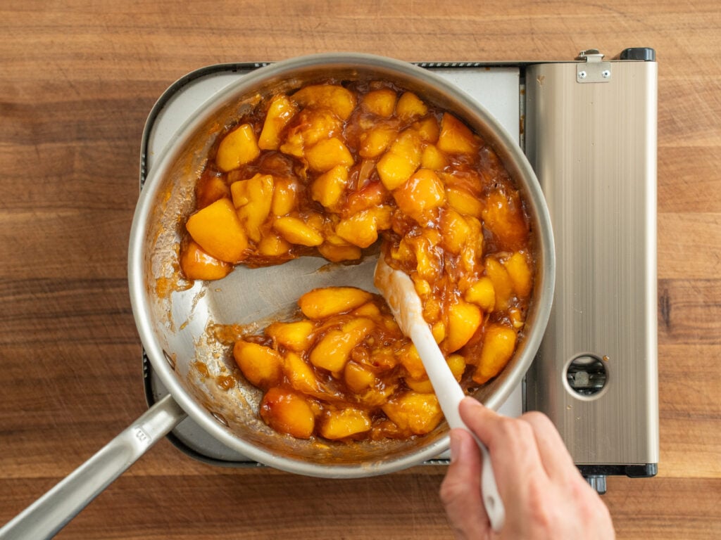 small white spatula leaves trail through peach filling cooking in silver pot