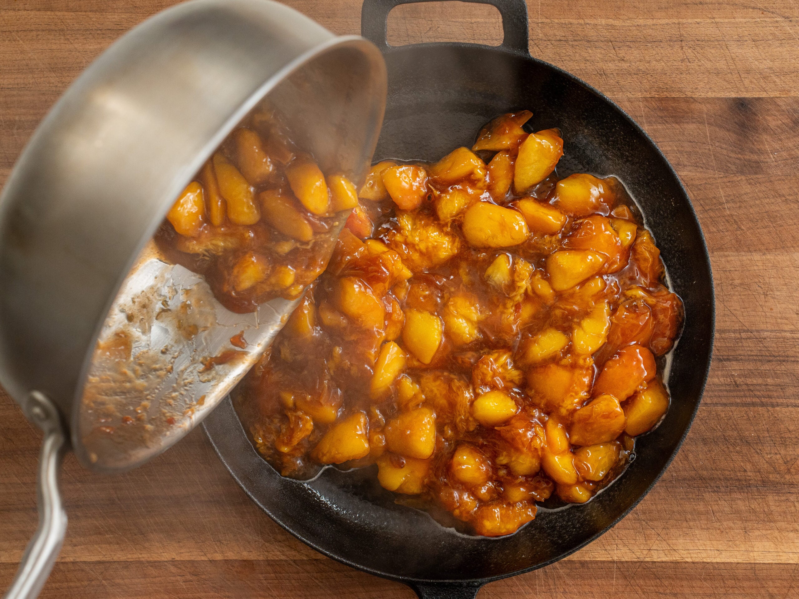 pouring pan of peach filling into black cast iron pan