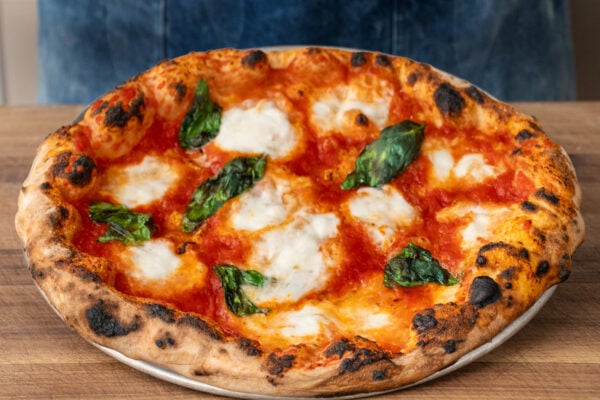 neapolitan pizza on wooden cutting board in front of blue apron