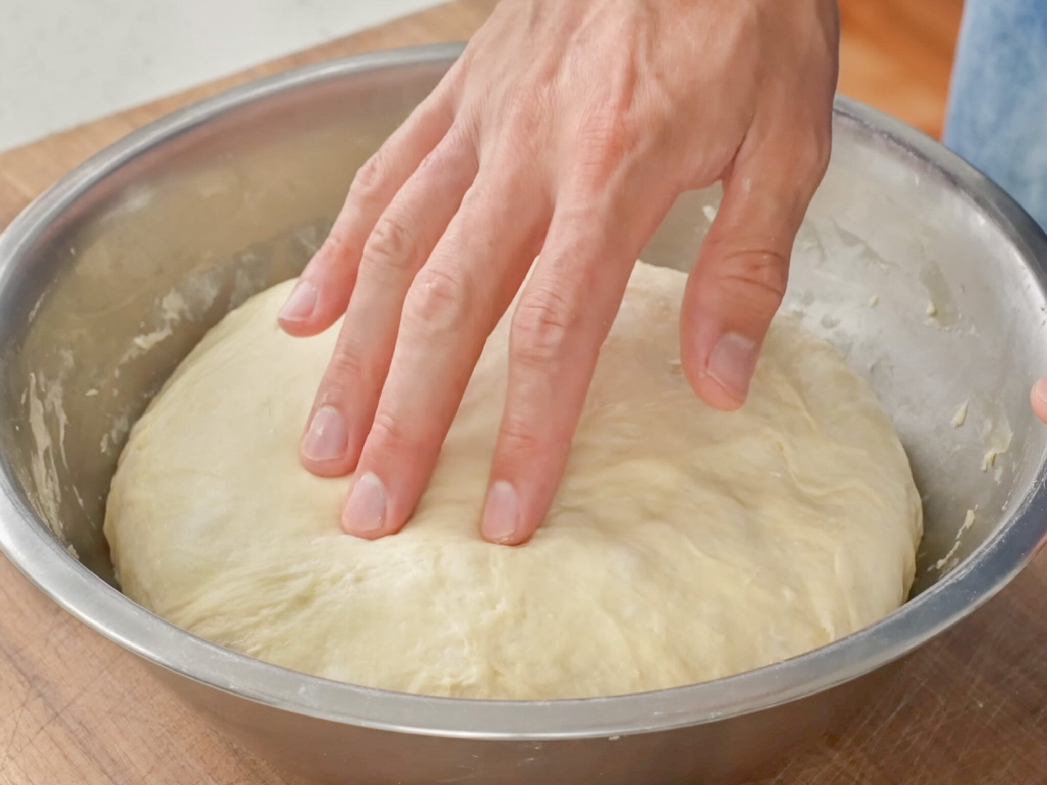 hand poking proofed dough ball in silver bowl