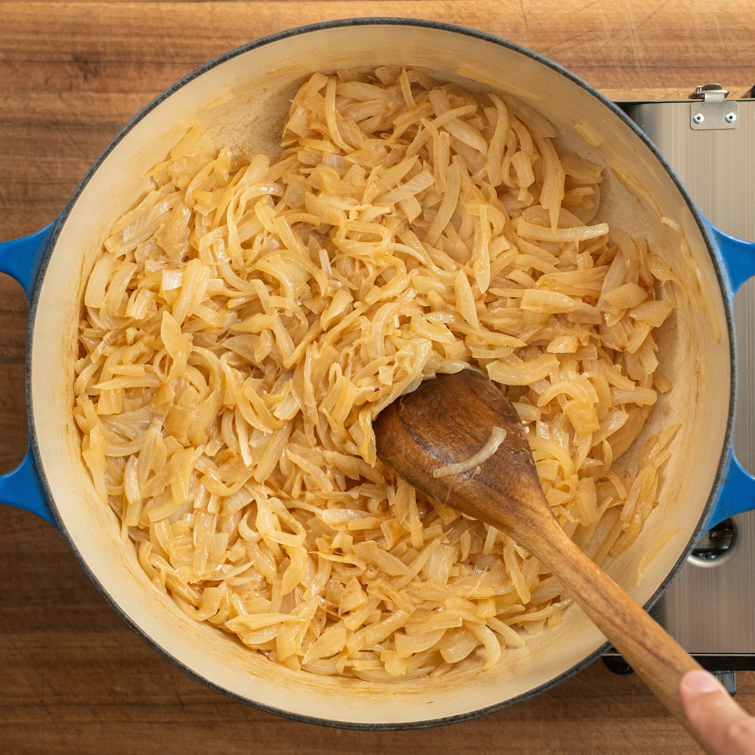 stirring browning onions in blue dutch oven with wooden spoon