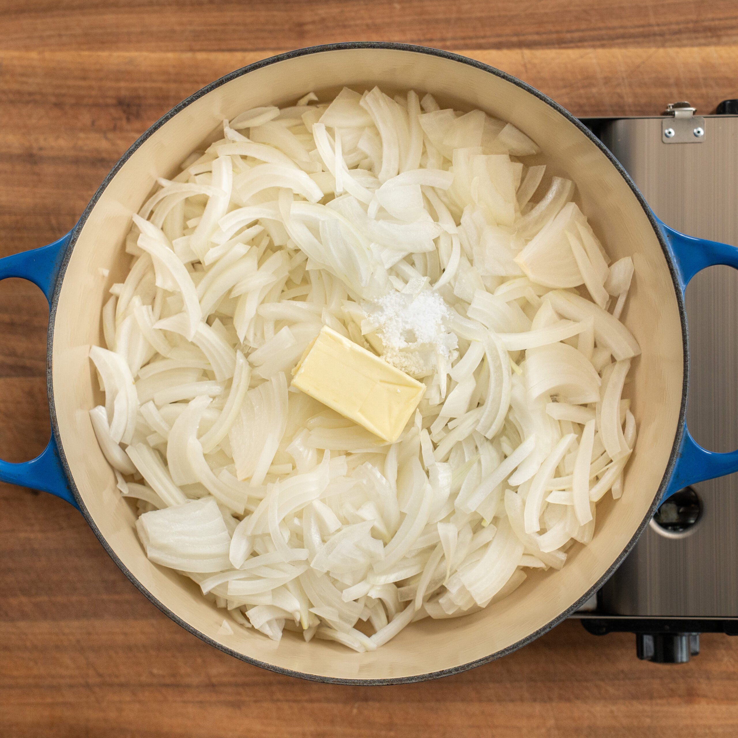 blue dutch oven filled with sliced onions and pad of butter