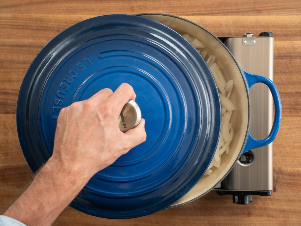 putting lid on blue dutch oven filled with sliced onions