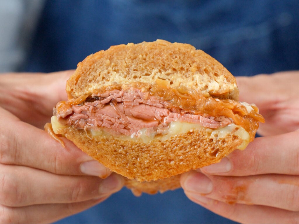 hands holding cross section of French dip sandwich on blue background