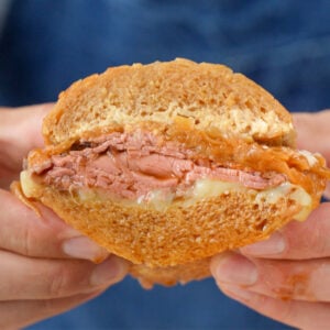 hands holding cross section of French dip sandwich on blue background