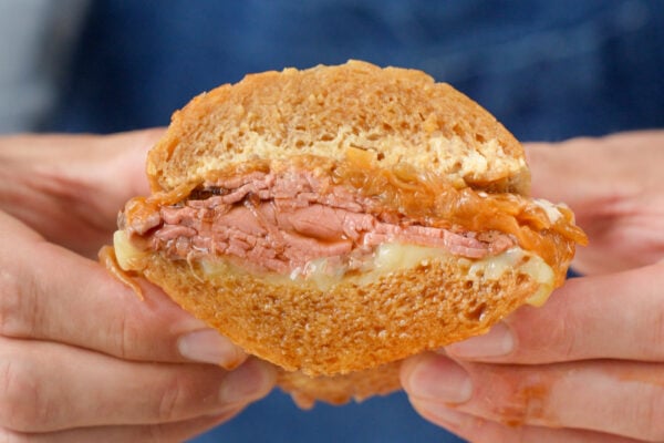 hands holding cross section of French dip sandwich on blue background