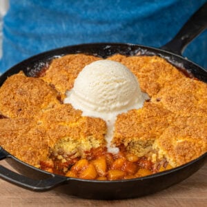 cast iron pan filled with peach cobbler topped with vanilla ice scoop